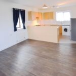 Open plan kitchen with white goods and living room with hard floors