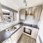 Kitchen with grey cupboards and tiles, including white goods