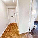 Hallway with wooden flooring and open door to room with carpet in rental property