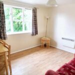 Furnished living room with red sofa, table with four chairs and end tables in apartment to rent near Milton Keynes